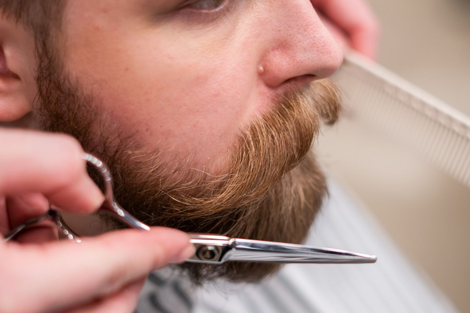 Barber trimming a man's full mustache with scissors and a comb, a classic look for Movember 2026 mustache grooming