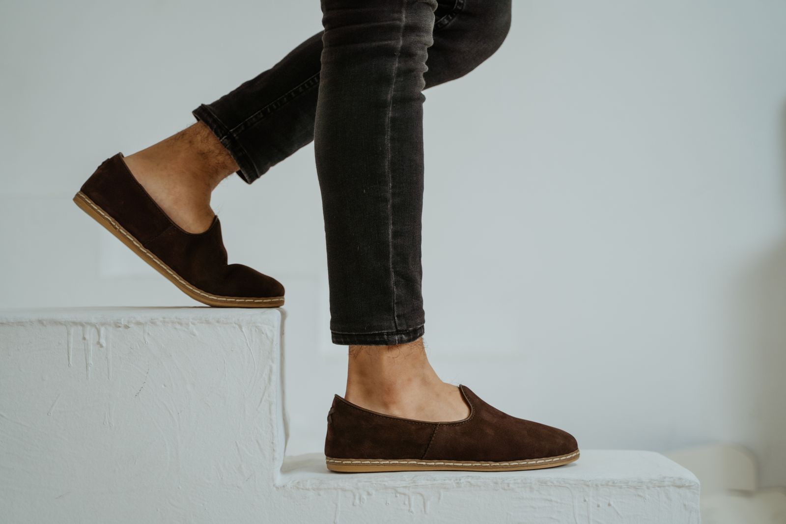 Man in dark jeans wearing chocolate brown suede loafers on white stairs, men's loafer trends fall 2026