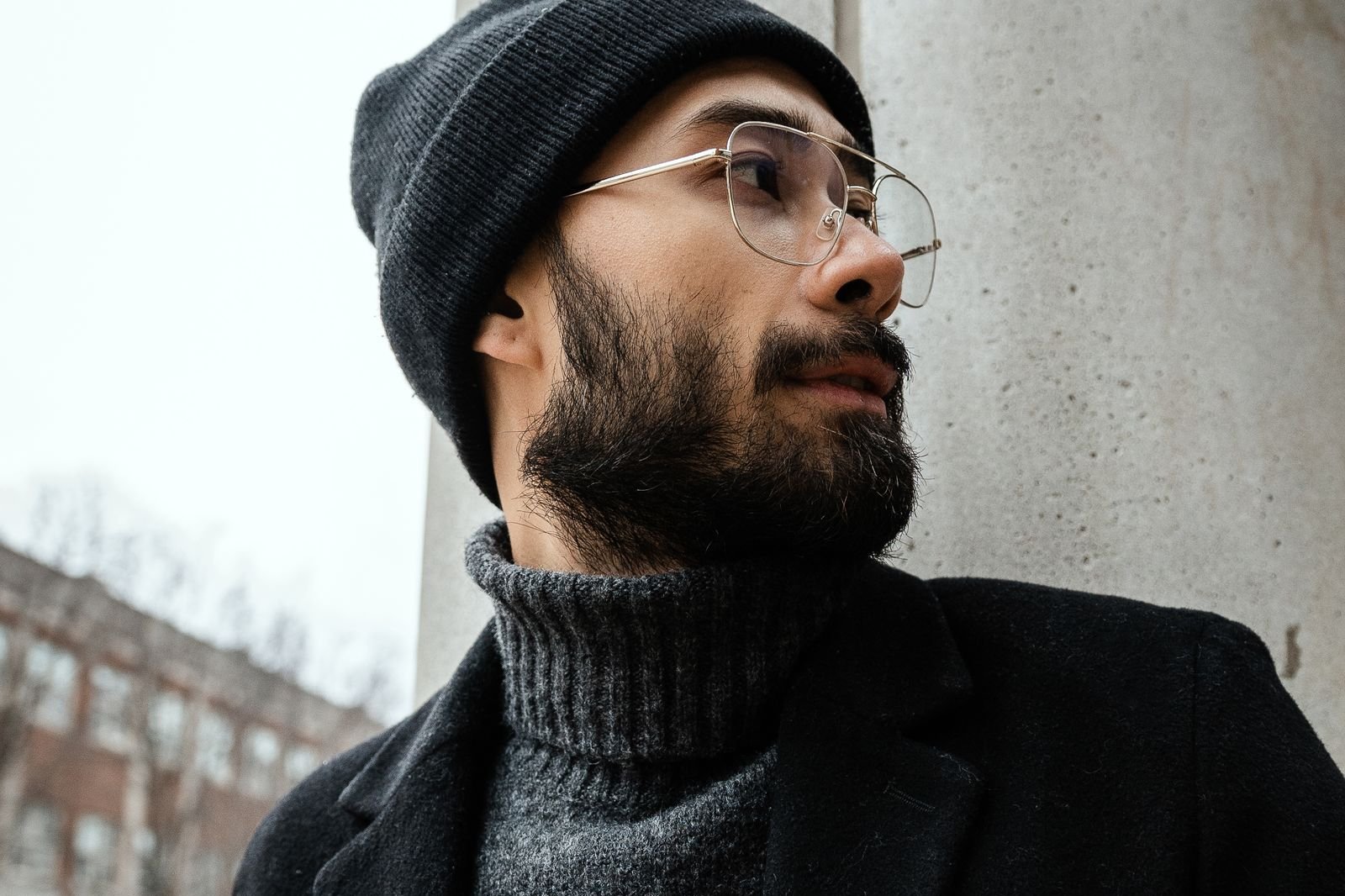 Bearded man in a black knit cap, charcoal turtleneck and black wool coat on a cold winter day, a stylish look for winter beard care