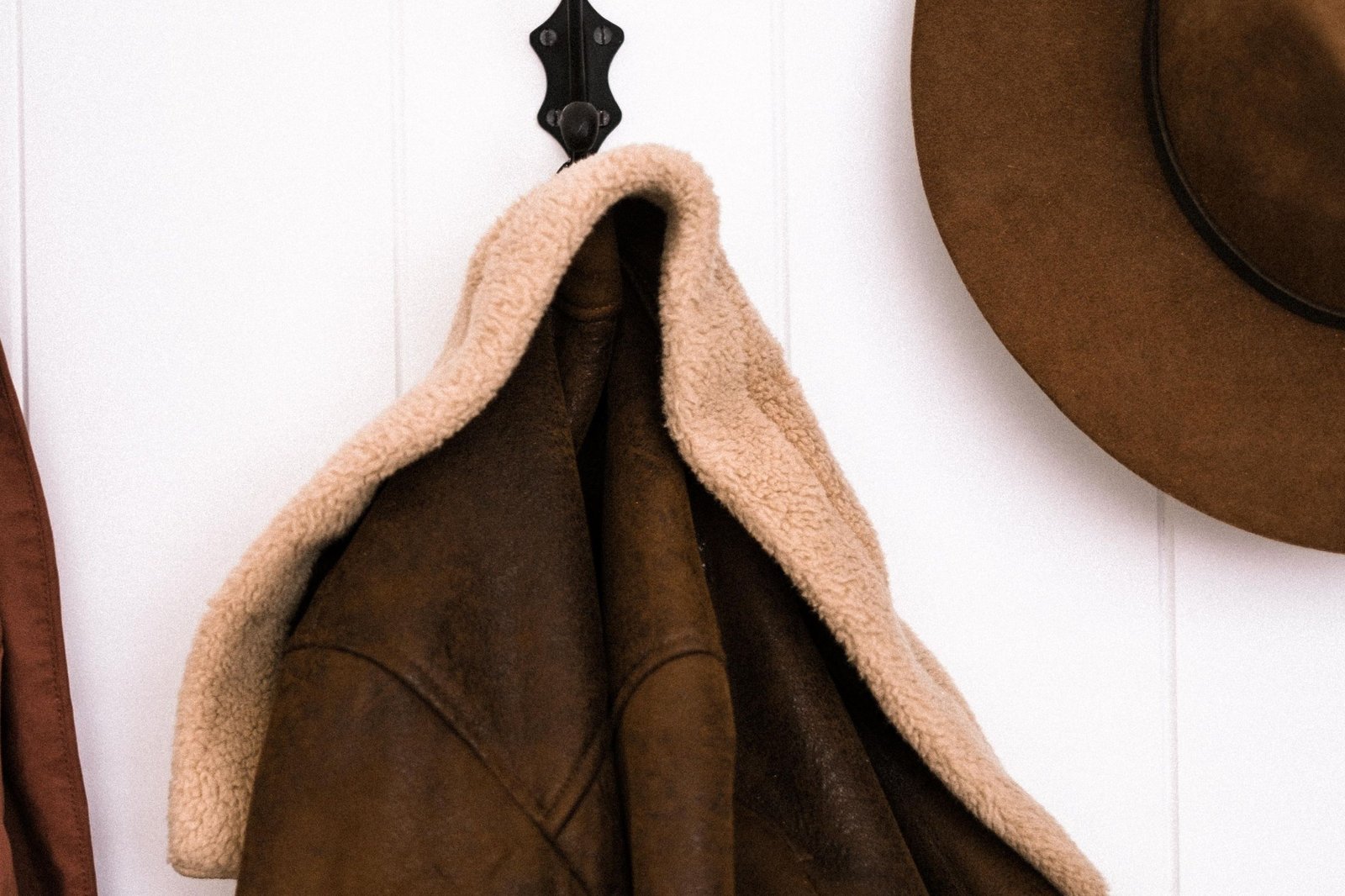 Men's leather jackets guide 2026: a brown shearling-collared leather jacket hanging on a wall hook beside a brown felt hat