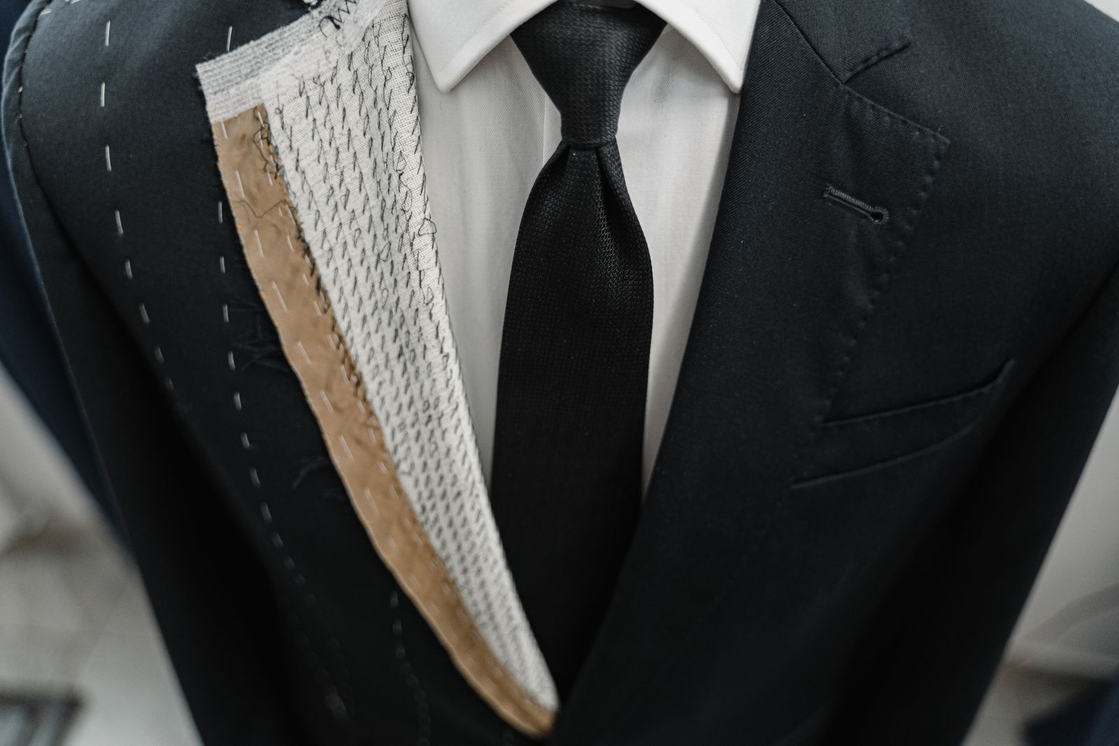 Close-up of a hand-basted bespoke suit jacket with exposed canvas and a dark knit tie, craftsmanship behind men's suit trends fall 2026