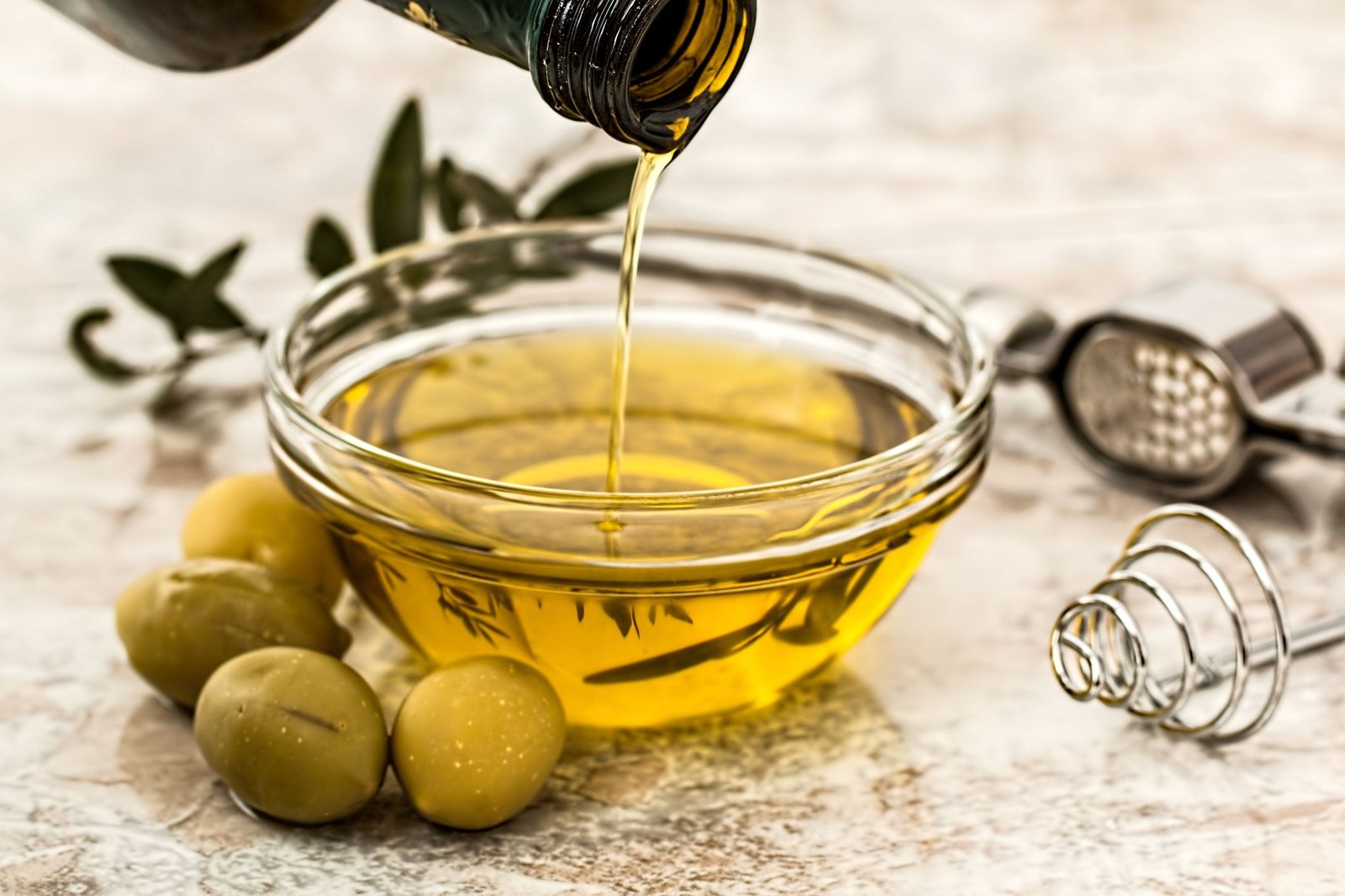 Extra virgin olive oil being poured into a glass bowl beside green olives, illustrating the heart-health benefits of olive oil and the Mediterranean diet for men